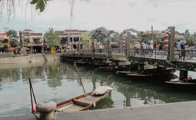 Imagen de Hoi An, muestra distintas balsas en el rio con edificios de la ciudad detrás